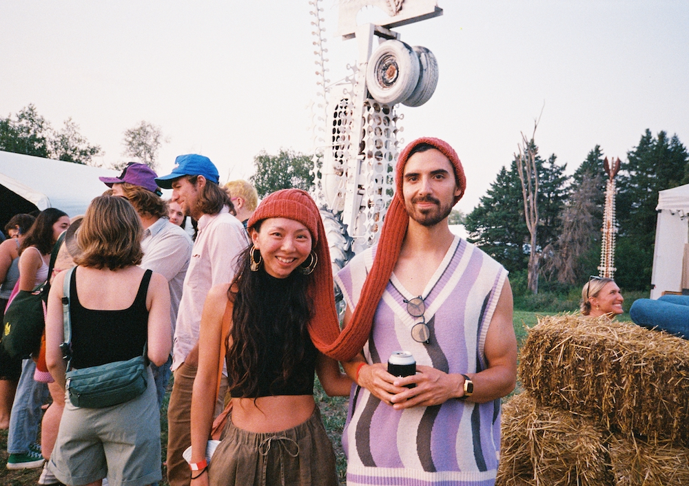 Two festival attendees pose and smile while wearing a tandem crocheted hat.
